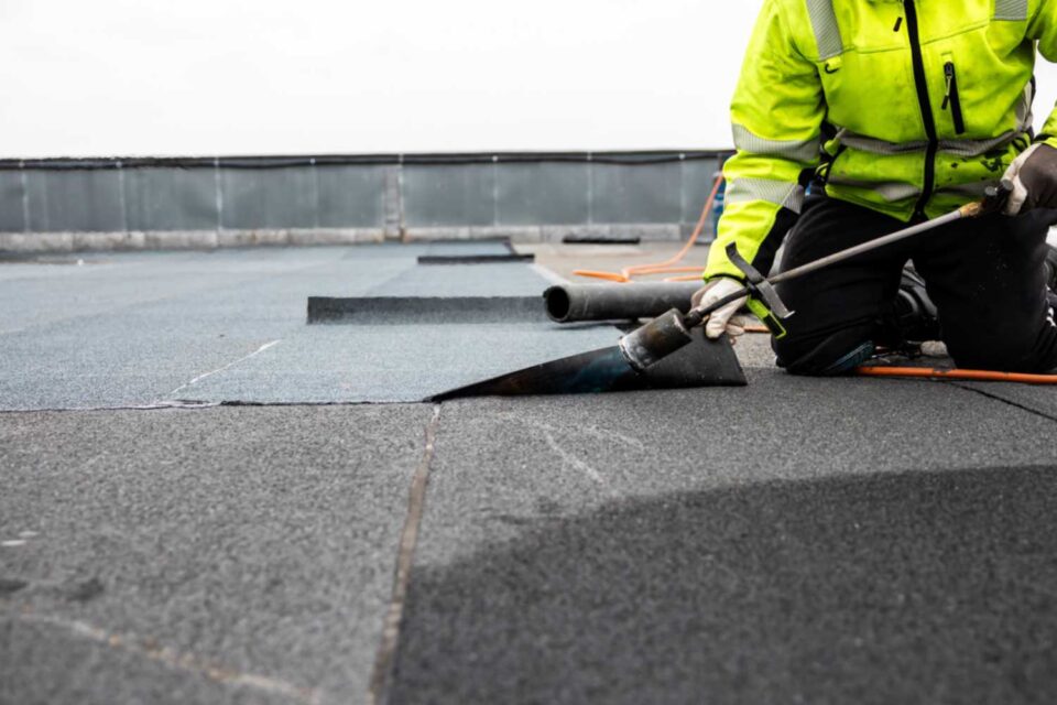 Roofer applying bitumen roll on flat roof on a commercial building in Denver, CO